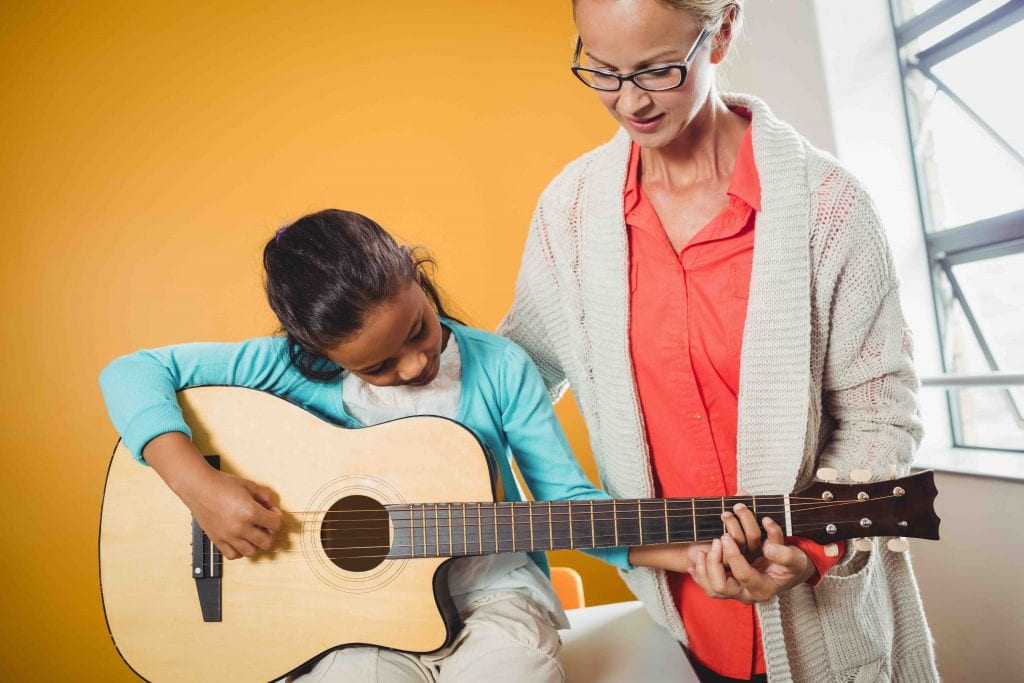 Girl learning how to play the guitar with the help of a teacher